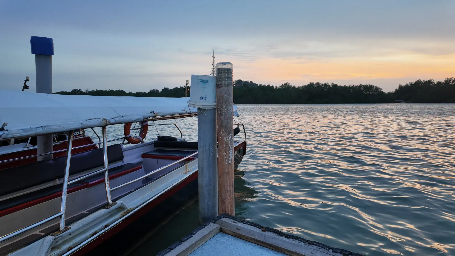 A covered electric firefly boat moored at the jetty at sunset