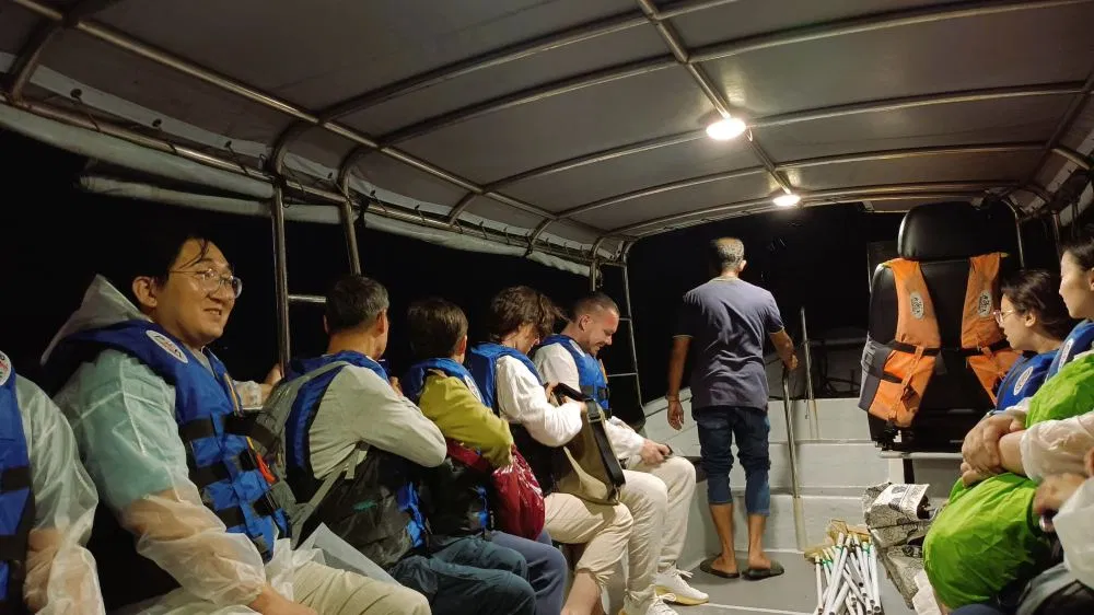 Passengers in life jackets seated inside a covered firefly boat at night